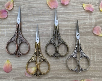 May include: Four ornate decorative scissors with intricate floral designs. The scissors are silver and gold in color and have a vintage aesthetic.