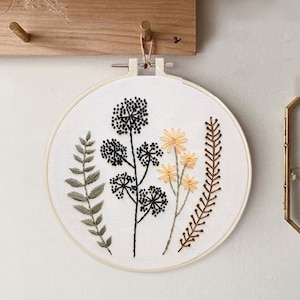 May include: Embroidered hoop art featuring a black floral design with yellow flowers and green leaves. The hoop is hanging on a wall.