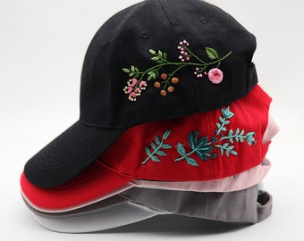 May include: A stack of four baseball caps with embroidered floral designs. The top cap is black with a green and pink floral design, the second cap is red with a green floral design, the third cap is pink, and the bottom cap is gray.