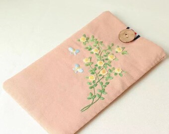 May include: A rectangular, blush-colored fabric case with an embroidered floral design. The embroidery features yellow roses, green leaves, and two blue butterflies. A wooden button secures the case's flap.