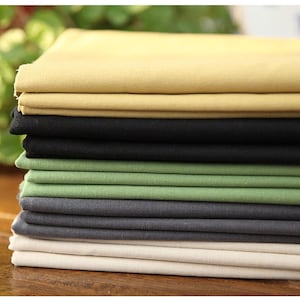 May include: A stack of folded fabric in various colors, including tan, black, green, gray, and off-white. The fabric appears to be a medium-weight material, suitable for sewing projects or crafting. The colors are solid and the fabric is neatly stacked.