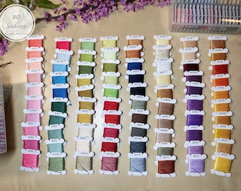 May include: A collection of 80 embroidery floss skeins in various colors, organized in rows and labeled with their corresponding numbers. The skeins are arranged in a rainbow pattern, starting with red and ending with yellow.