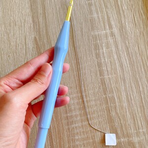 May include: A light blue plastic yarn needle with a gold metal tip and a thin silver thread attached.
