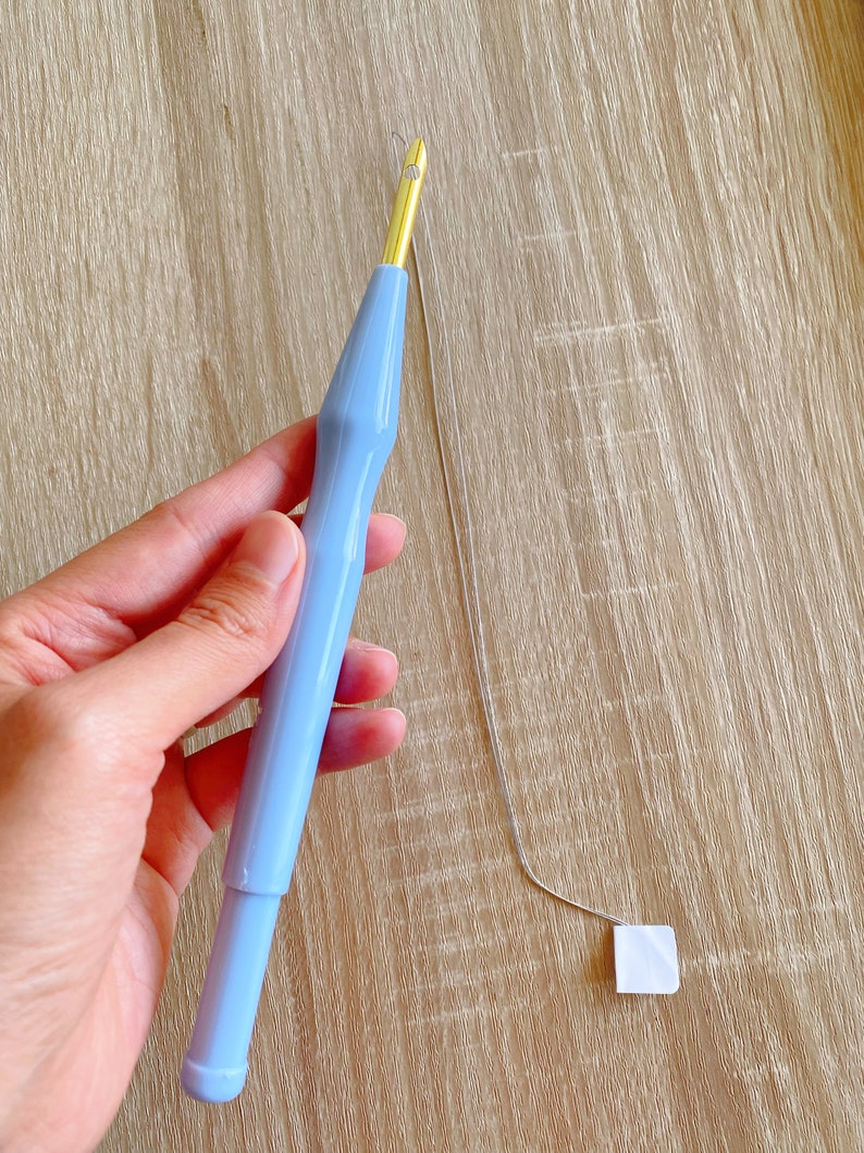 May include: A light blue plastic yarn needle with a gold metal tip and a thin silver thread attached.