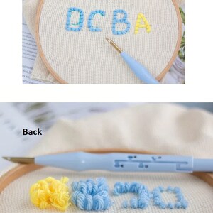 May include: Close-up of a embroidery hoop with the letters DCBA stitched in blue thread. The back of the hoop shows four different colored yarn pom-poms labeled A, B, C, and D.