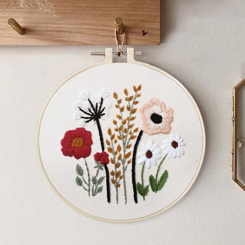 May include: Embroidered hoop art featuring a floral design with red, white, and pink flowers, green leaves, and brown stems. The hoop is white and has a wooden frame.