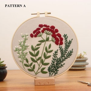 May include: Embroidered hoop art featuring a red flower with green leaves and stems. The hoop is made of wood and has a beige fabric background. The text "PATTERN A" is visible at the top of the image.