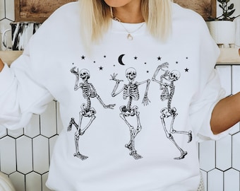May include: White sweatshirt with a graphic of three skeletons dancing under a crescent moon and stars. The skeletons are black and white and have a whimsical look.