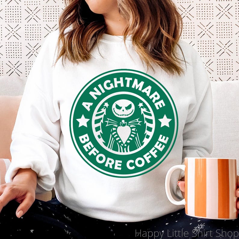 Pu&ograve; includere: Felpa bianca con una grafica verde e bianca che recita "A Nightmare Before Coffee". La grafica presenta un'immagine stilizzata di Jack Skellington di The Nightmare Before Christmas. Una tazza a righe arancioni e bianche &egrave; tenuta in mano.