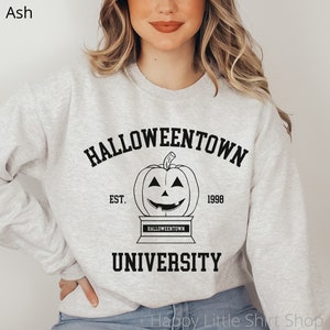 Puede incluir: Una sudadera gris con un estampado gr&aacute;fico negro que dice "Halloweentown University" con una calabaza y el texto "Est. 1998".