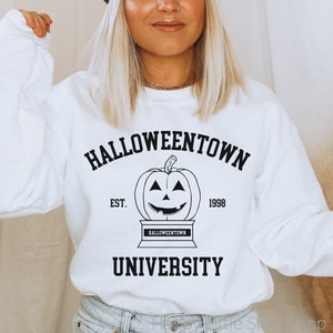 Puede incluir: Sudadera blanca con texto negro que dice "Halloweentown University Est. 1998" con una ilustraci&oacute;n en blanco y negro de una calabaza de Halloween.