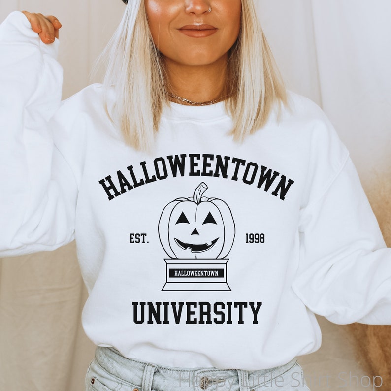 Puede incluir: Sudadera blanca con texto negro que dice "Halloweentown University Est. 1998" con una ilustraci&oacute;n en blanco y negro de una calabaza de Halloween.