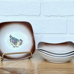 May include: Set of four brown and white ceramic square bowls with a rooster design. The bowls are stacked on top of each other.