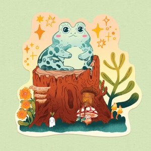 May include: A whimsical illustration features a light blue frog with dark spots sitting on a tree stump. The scene includes an acorn character, mushrooms, flowers, and a small ghost-like figure, all set against a soft green background with sparkling accents.