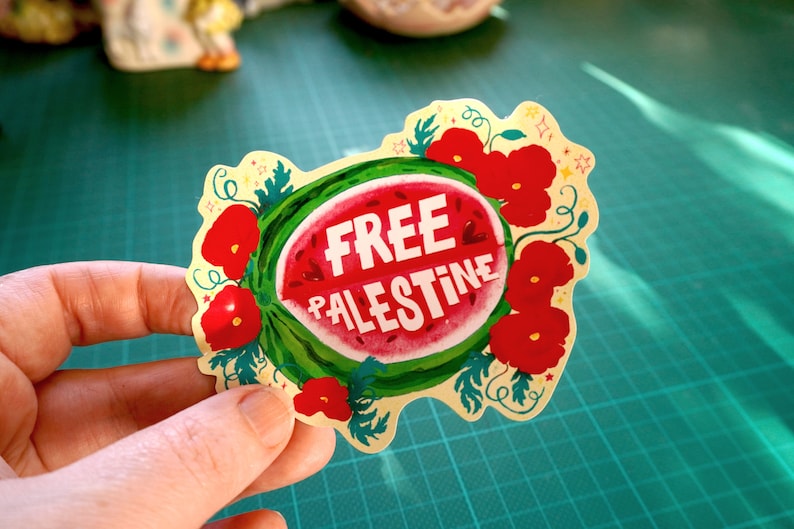 Peut inclure: Autocollant avec une tranche de past&egrave;que et l'inscription "FREE PALESTINE" en blanc. Des coquelicots rouges et des feuilles vertes entourent la past&egrave;que. Le bord de l'autocollant est festonn&eacute; avec de petites &eacute;toiles.