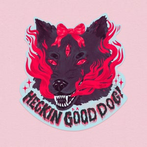 Puede incluir: Una pegatina con una ilustración estilizada de un perro negro con tres ojos y un lazo rojo. Llamas rojas y el texto "HECKIN GOOD DOG!" rodean la cabeza del perro. La pegatina tiene un borde azul claro sobre un fondo rosa.
