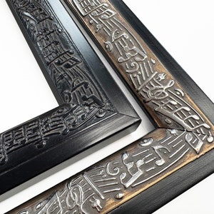 May include: Two black picture frames with a decorative border of musical notes. The top frame has a black border with silver musical notes. The bottom frame has a gold border with silver musical notes.