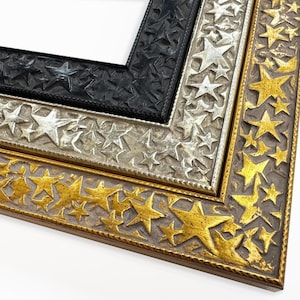 May include: Three picture frames with a star design. The outer frame is gold, the middle frame is silver, and the inner frame is black.