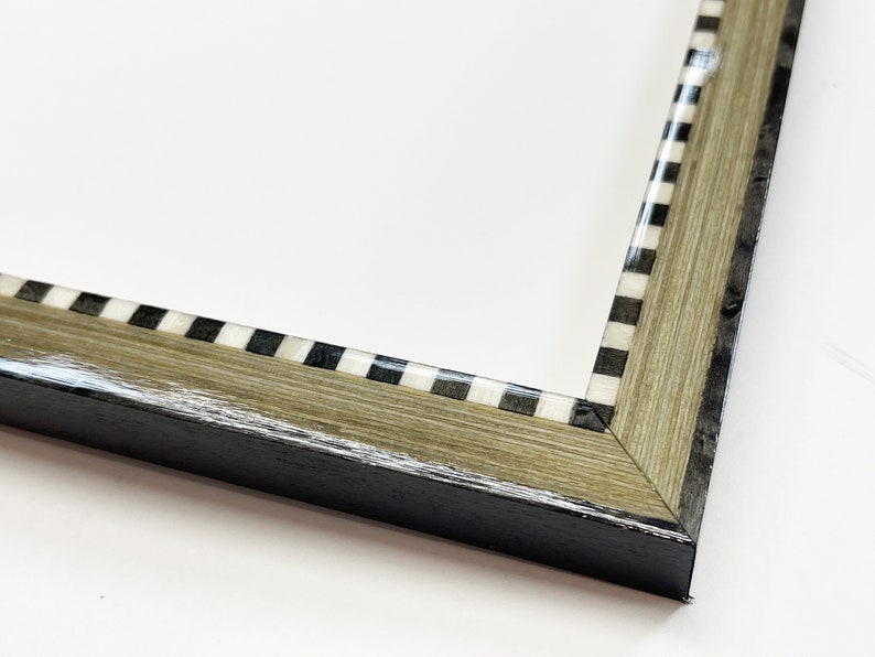 May include: Close-up of a picture frame with a black and white checkered border. The frame is made of wood with a light brown stain and a black outer edge.