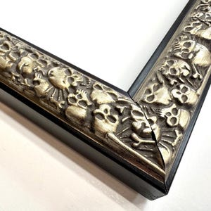 May include: Close-up of a black picture frame with a silver ornate design featuring skulls and other decorative elements. Skulls Gothic Picture Frames Silver Black Eclectic Unique Photo Display Metallic Wood  Gift Wall Deco 4x6 5x7 8x10 11x14 16x20 18x24