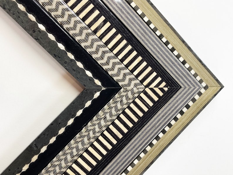 May include: Close-up of a corner of a decorative picture frame with a multi-layered design. The frame features a black, white, and gray geometric pattern.