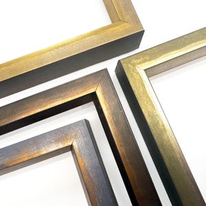 May include: Close-up of four picture frames with a metallic finish. The frames are in shades of gold, bronze, and dark brown, with visible wood grain texture. The corners of the frames are joined at right angles.