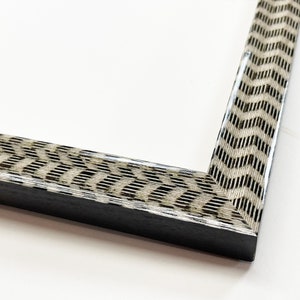 May include: A close-up of a black picture frame with a white and brown patterned border. The frame has a simple, modern design.
