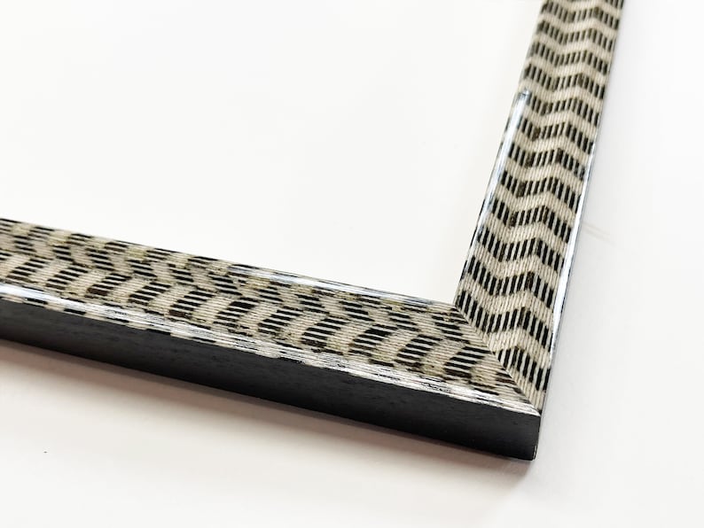 May include: A close-up of a black picture frame with a white and brown patterned border. The frame has a simple, modern design.