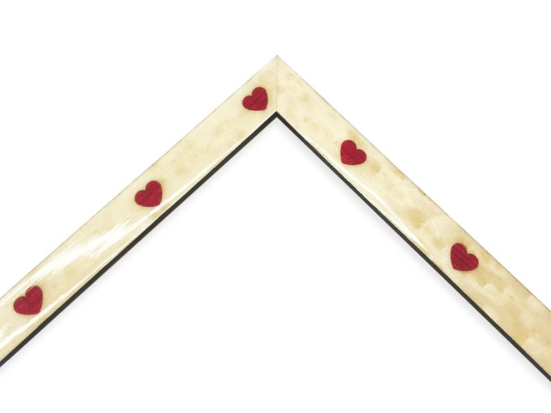 May include: A corner of a picture frame with a light beige finish and a black interior edge. Small red heart-shaped embellishments are evenly spaced along the frame's edge. The frame is set against a white background.