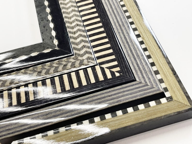 May include: Close-up of a multi-layered picture frame with a black, white, and gray geometric pattern. The frame is made of wood and has a glossy finish.