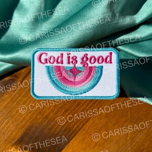 May include: White embroidered patch with a blue border and a rainbow design. The text "God is good" is written in black letters on the patch.