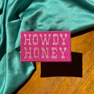 May include: Pink fabric patch with white embroidered text that reads "Howdy Honey".