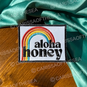May include: A white patch with a rainbow and the text "aloha honey" in black letters.