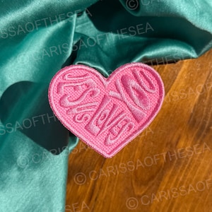 May include: Pink felt heart-shaped patch with the text "I love you" in a stylized font.