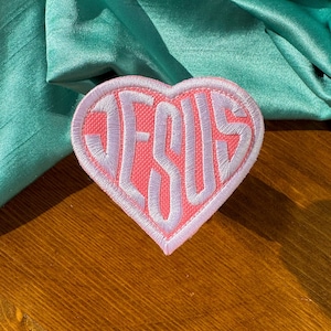 May include: Pink heart-shaped patch with white embroidered lettering that says "JESUS".
