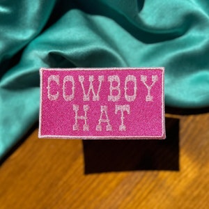 May include: Pink fabric patch with white embroidered text that reads "COWBOY HAT".