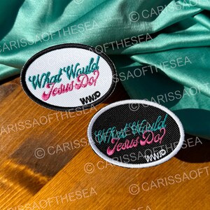 May include: Two black and white embroidered patches with the text "What Would Jesus Do?" and the acronym "WWID" in pink. The patches are on a wooden surface.