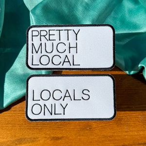 May include: Two white iron-on patches with black text. The top patch says "Pretty Much Local" and the bottom patch says "Locals Only".