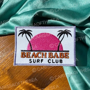 May include: A white patch with a pink sunset, two palm trees, and the text "Beach Babe Surf Club".