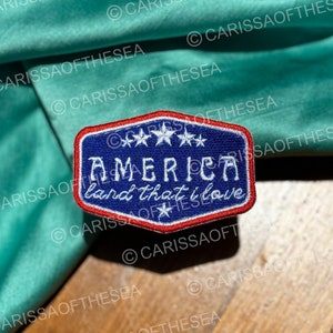May include: A blue and red embroidered patch with white stars and the text "America land that I love".