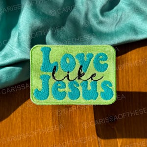 May include: Green and blue embroidered patch with the text "Love like Jesus" in a retro font.