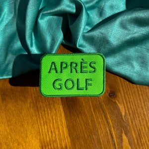 May include: A green embroidered patch with the text "APRÈS GOLF" in black.