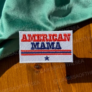 May include: White embroidered patch with red, white, and blue stripes and a star. The patch says "AMERICAN MAMA" in blue lettering.