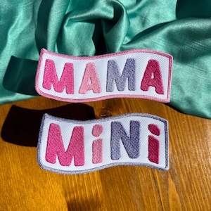 May include: Two white fabric patches with pink and purple embroidered letters. The top patch says "MAMA" and the bottom patch says "MINI".