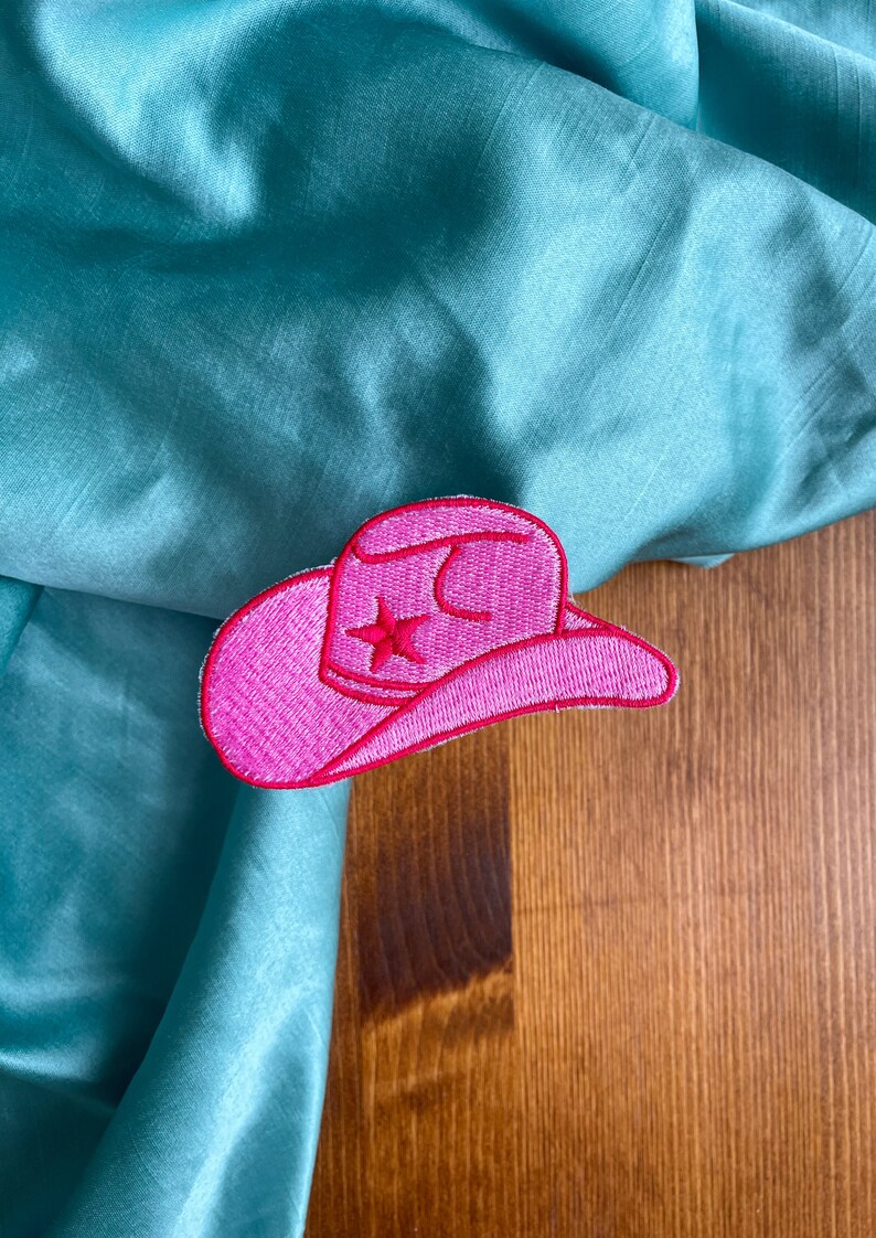 May include: Pink felt cowboy hat patch with a white star on a teal fabric background.