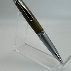 May include: A silver and wood pen with a silver clip and a silver tip. The pen is on a clear acrylic stand.