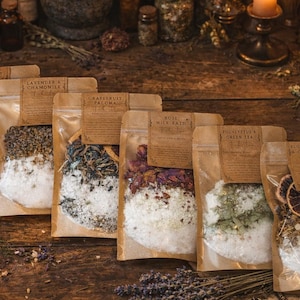 May include: Several bath salt pouches with brown paper labels, including "Lavender & Chamomile" and "Eucalyptus & Green Tea". The pouches are filled with salts and botanicals. The image is set on a rustic wooden surface.