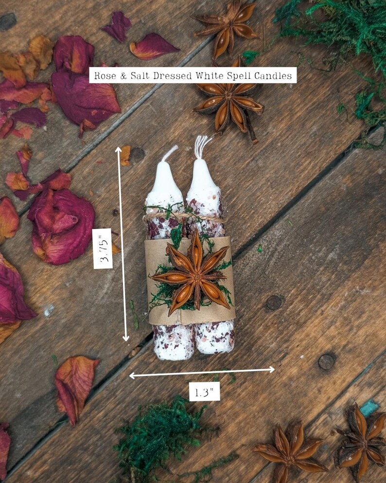 May include: Two white spell candles, 3.75 inches tall and 1.3 inches wide, are wrapped together with a brown paper band, dried roses, and star anise. The candles are decorated with rose petals and salt. The text on the image reads "Rose & Salt Dressed White Spell Candles."