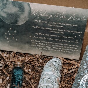 May include: A box with instructions for making moon water. The box contains a white sage smudge stick, a small glass bottle with blue crystals, and a piece of paper with instructions on how to make moon water.