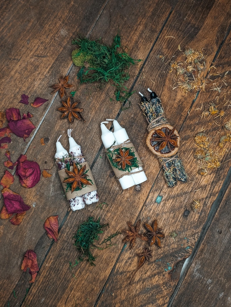 May include: An overhead shot of three sets of white candles, each bundled and decorated with star anise, twine, and greenery. Dried rose petals and star anise are scattered on the wooden surface, creating a rustic, natural aesthetic.
